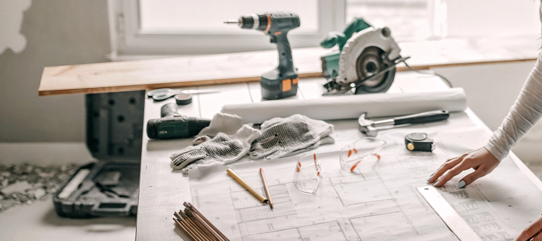 A contractor looking at a tabletop with power tools and blueprints spread across it.